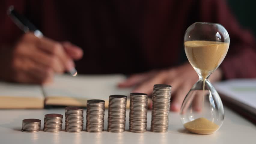 Coin stacks and sand clock on the table. Growing of income, saving or return investment through time. Time and money concept.
