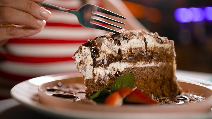 A close-up of a fork taking a piece from a rich spongy chocolate cake on a plate