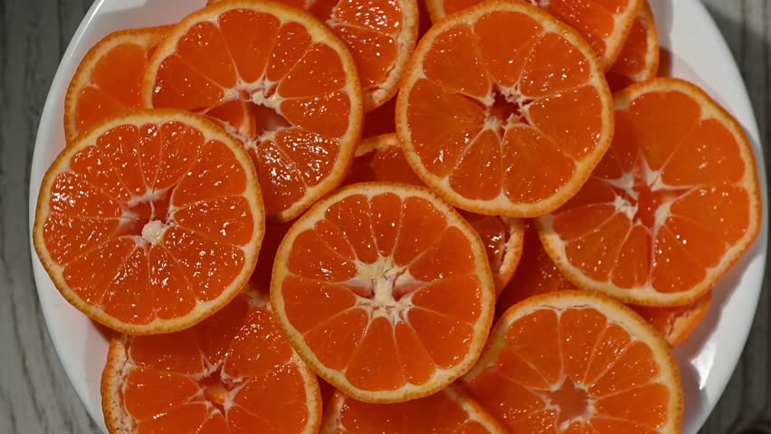 A continuous, seamless 4K video loop of mandarin slices rotating in a rhythmic pattern on a dark surface. Created specifically as a versatile, non-distracting yet engaging motion background. The vibrant orange color and organic shapes provide warmth and energy, making it perfect for overlaying text in cooking tutorials, health seminars, website banners, YouTube intro outro sequences, or as a dynamic visual element in digital advertising and social media content.