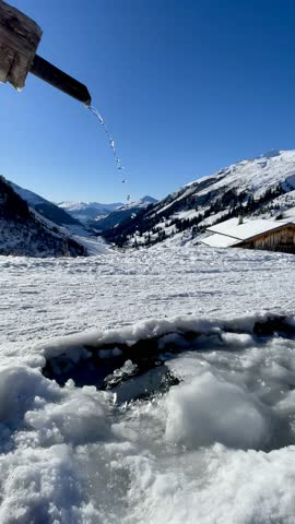 Frozen fountain basin with dripping water set against a cold winter landscape. Grisons, Switzerland.