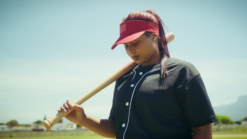 Focused female baseball player stands ready. She holds her bat, exuding determination and readiness for competition.