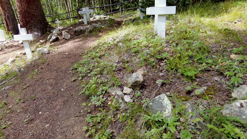 Unmarked graves mark the burials of the pioneers of an old silver mining boom town in Colorado. Walking downhill next to the rows of burials and white wooden crosses with no names.