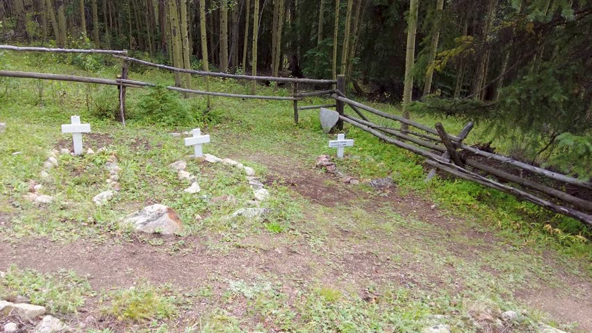 Unmarked wooden cross headstones mark the burials of the wild west pioneers who came to the mountains of Colorado during a mining boom only to reach a tragic fate.  Pan from right to left uphill. 