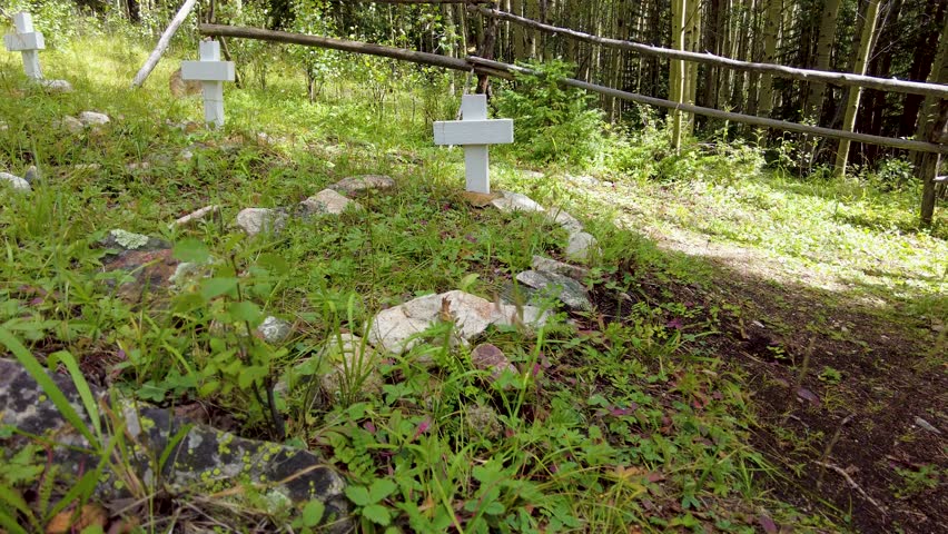 Unmarked graves with wooden crosses fill this old historic graveyard in the mountain forest outside an old mining boomtown in Colorado.  Walk by multiple burials uphill original color.