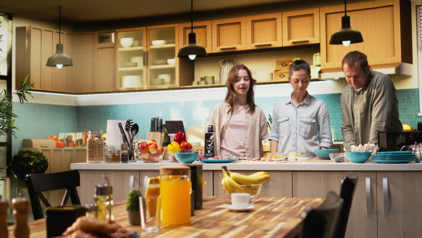 Pre-teen daughter taking pictures of her and parents preparing pizza together, making memories through fun weekend activity. Girl takes a family photo in the kitchen, bonding. Camera A.