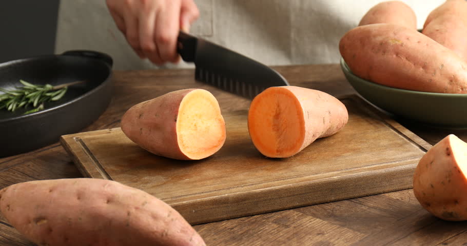 Woman cutting sweet potato at wooden table, closeup