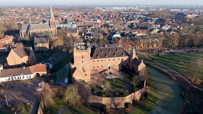 Aerial view of Dutch town red brick castle with moat, church spire, dense homes, and distant wind turbines blend medieval heritage with modern sustainability.