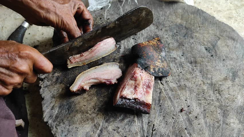 A person is cutting bacon on a round wooden cutting board. 