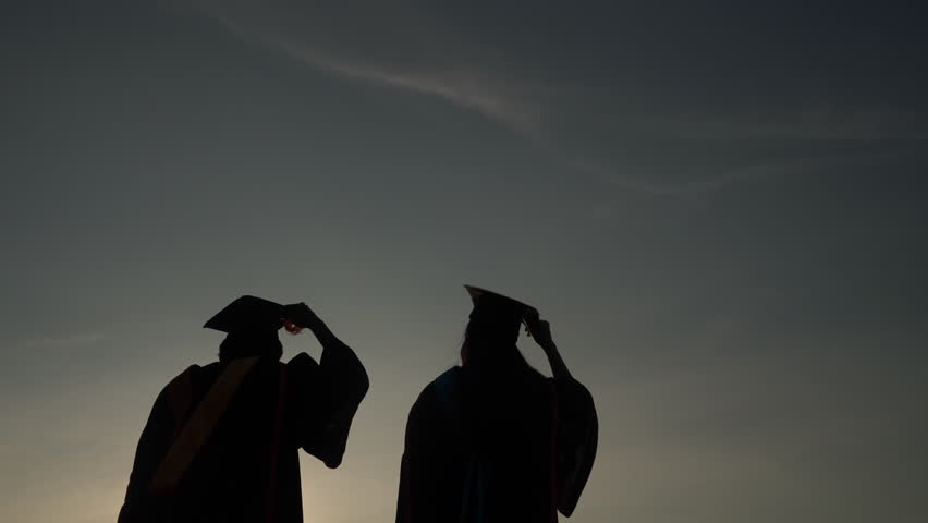 Silhouette of joyful graduates raising diploma and graduation cap into the air at dusk, expressing freedom, celebration, and academic success.