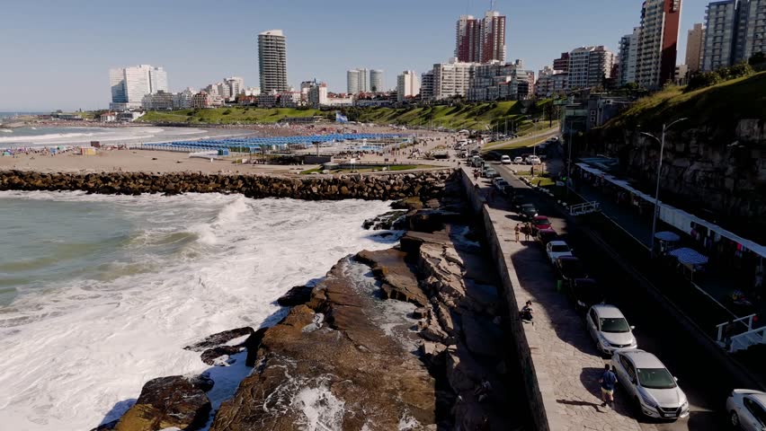 Enjoying a sunny summer day at Varese beach in Mar del Plata, Argentina. The camera performs a push in movement from a high angle view over the rocks
