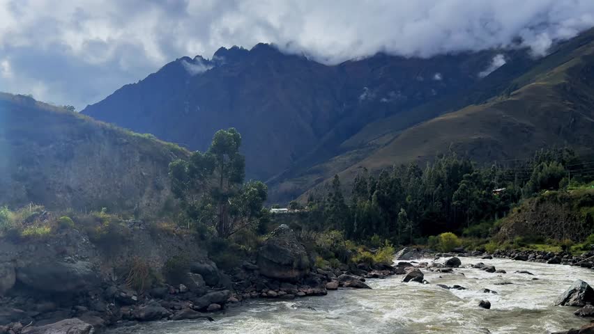 Urubamba river high flow Peru Rail train Inca Trail Ollantaytambo in route Aguas Calientes Machu Picchu Peruvian Andes mountains range peaks rainy season sunny blue sky clouds Amazon forward motion