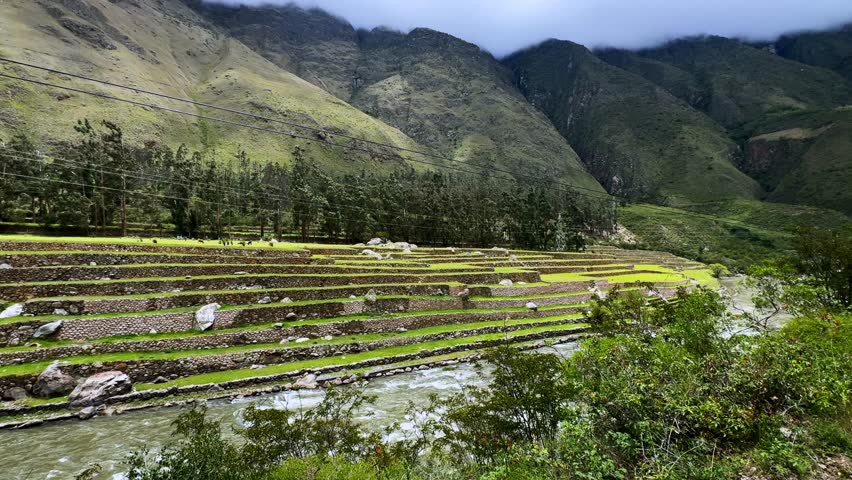 Peru Rail train Inca Trail terrace sites Ollantaytambo in route Aguas Clients Amazon Urubamba river Machu Picchu Peruvian Andes mountains range peaks rainy season sunny blue sky clouds power lines pan