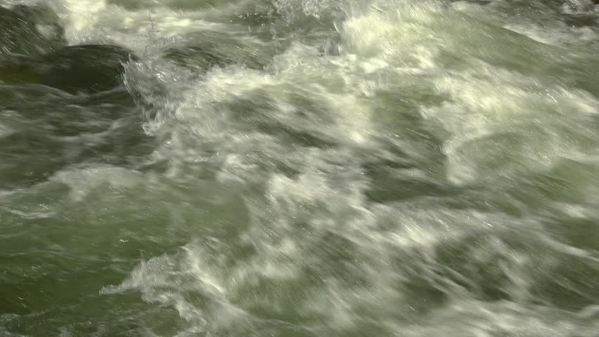 A close-up of rapids with white caps flowing quickly on a raging river during a sunny day.