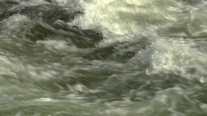 A close-up of rapids with white caps flowing quickly on a raging river during a sunny day.