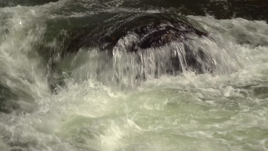 A close-up of water pouring over a rock on a river with rapids during a sunny day.