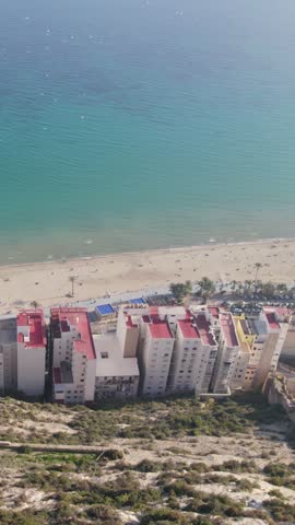Vertical aerial view of Alicante’s coastline and harbor with clear blue water and gentle morning light, Spain.