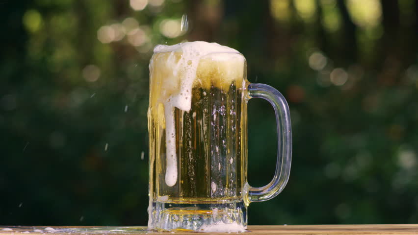 Beer pours slowly with beerfoam. Beer pour in glass sparkles with bubbles. Beer on outdoor summer background. Beer pour in beerglass closeup.