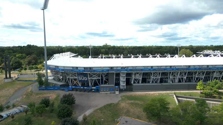 Low altitude pullback of Montreal olympic stadium surrounded by trees, roads, and city buildings, establishing overview