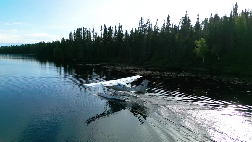 Seaplane gliding across glassy water with foggy forest shoreline, drone rearview establish nature scenery