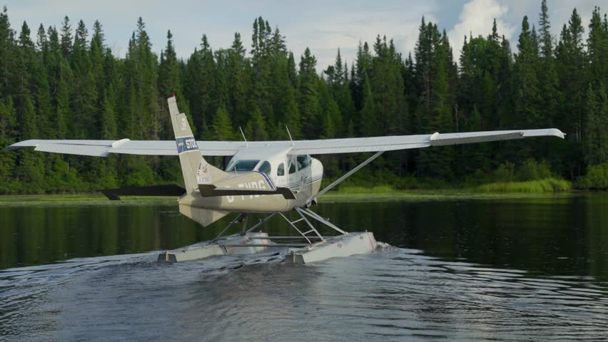 Seaplane floatplane moving slowly on lake framed by dense boreal forest, propellor spins in slow motion, Seignurie Du Triton Quebec Canada