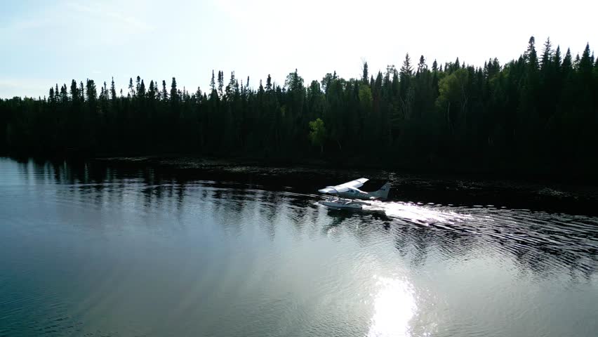 Aerial of seaplane touching down on calm lake surrounded by misty forest in Quebec wilderness, rearview follow