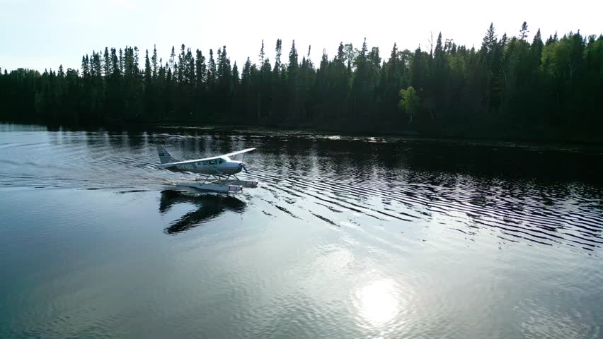 Cinematic aerial tracking follow seaplane slows on water leaving ripples through foggy forest lake, rearview medium approach to pier