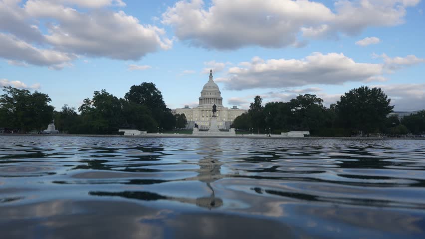 Washington DC Capitol reflected in calm water. US Capitol building in Washington DC. United States Capitol under blue sky. Washington DC Congress landmark view. American Capitol with water reflection.