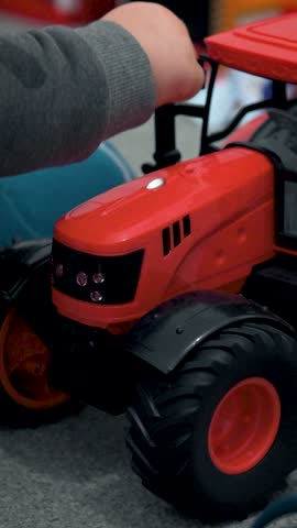 Vertical close-up video of a child engaging with a red toy tractor. This intimate view of playtime is ideal for social media content related to parenting, child development, and toy reviews.