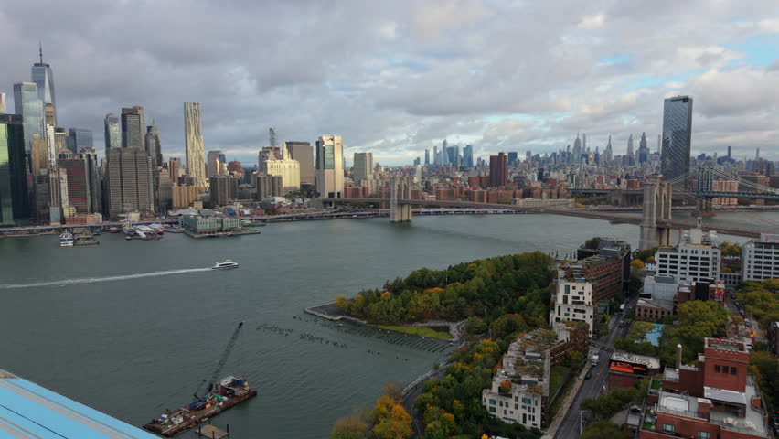 Cinematic aerial view of Manhattan skyline with Brooklyn bridge, New York City skyscrapers along the river, showing dense urban architecture, financial district atmosphere and iconic New York.