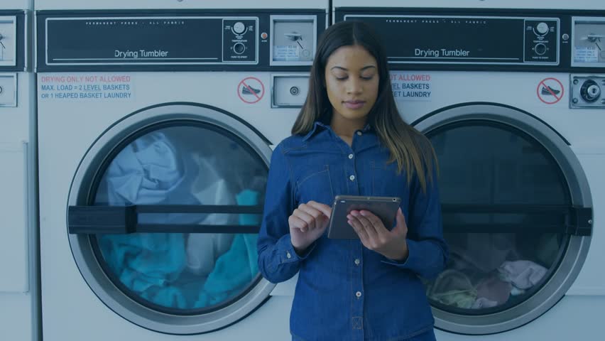 Composite video of young woman using tablet pc at laundromat and eye icon. Technology, convenience, laundry, computer graphic, lifestyle, connection, watching.