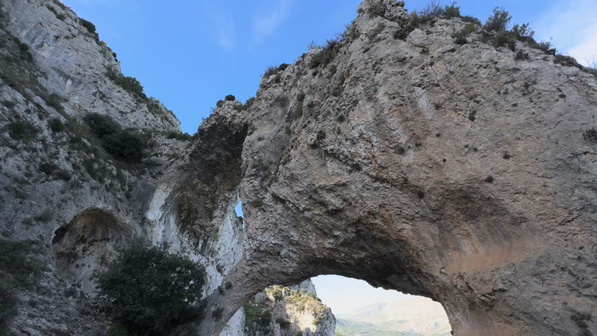 Time-lapse of a rugged limestone rock arch in the mountains as daylight softens, revealing rich textures, distant peaks and a quiet valley below.
