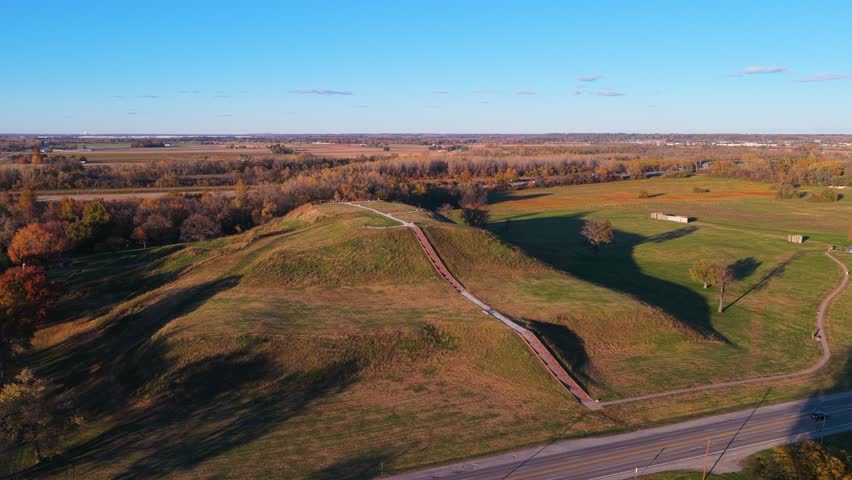 Cinematic drone footage orbiting Monk’s Mound at Cahokia Mounds, revealing all sides of the historic landmark. Autumn trees surround the site beneath a clear blue sky.