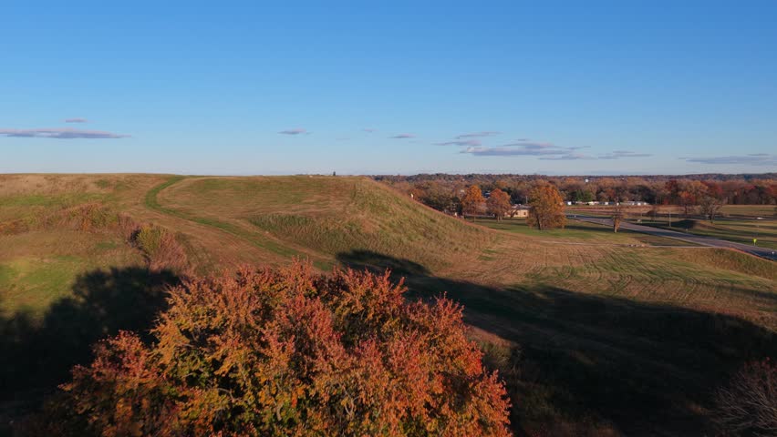 Drone footage flying up and over Monk’s Mound at Cahokia Mounds as visitors climb the stairs below. Colorful autumn trees surround the historic site under a bright blue sky.