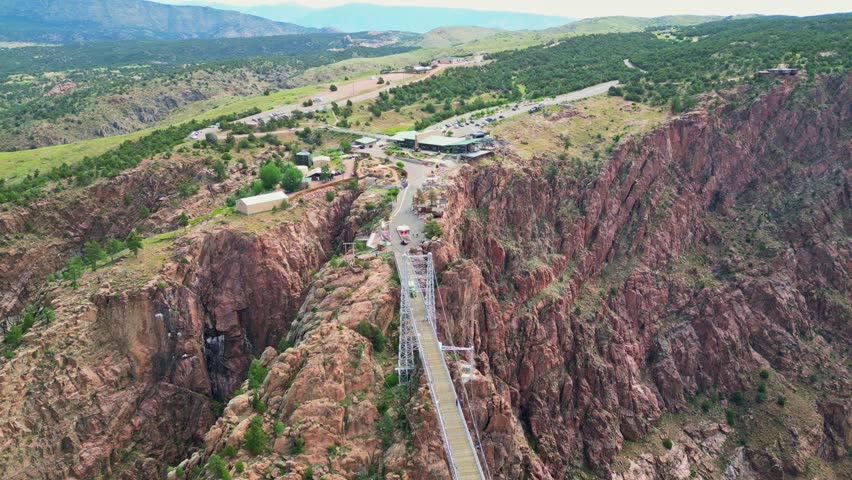 An impressive aerial shot captures the iconic Royal Gorge Bridge spanning the deep canyon in Colorado, with the Royal Gorge Bridge and Park visitor center and surrounding rugged landscape visible in