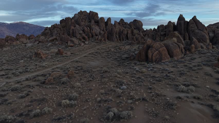 Horizontal 4K real-time drone footage flying backward over the boulders of Alabama Hills, California. The clip showcases the rugged desert landscape, dramatic rock formations, and natural scenery, highlighting the expansive wilderness and beauty of the Eastern Sierra region.
