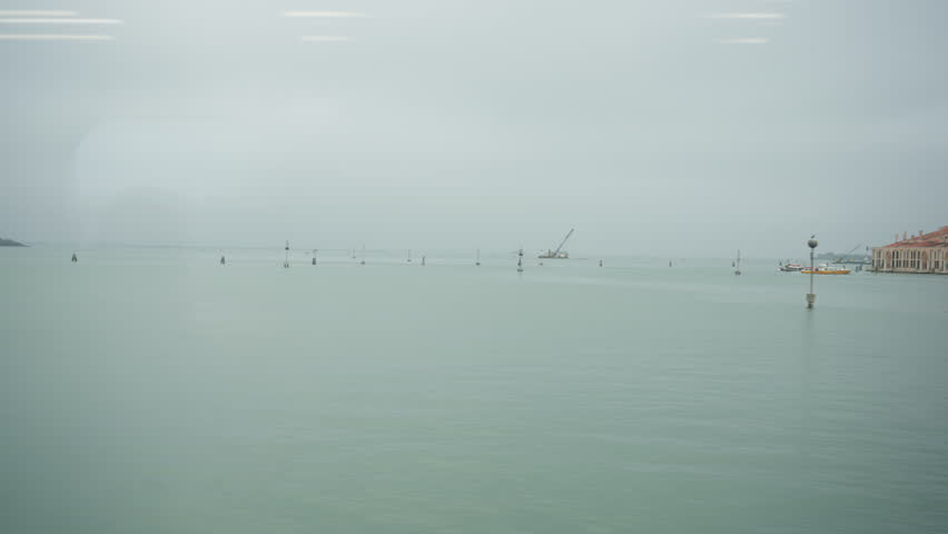 Moving train window view of Venice Santa Lucia arrival. Water taxis and boats navigate the busy canal hub towards the station. Transportation and travel logistics in the Venetian lagoon.