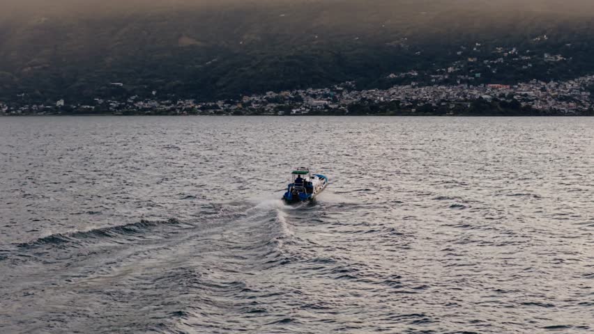 Drone view of small boat moving across Lake Atitlan with misty mountains