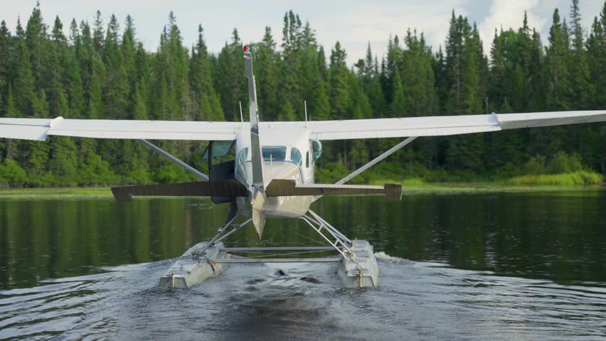 Seaplane driving across open lake water with forest shoreline in quiet quebec wilderness, rearview slow motion, Seignurie Du Triton Quebec Canada