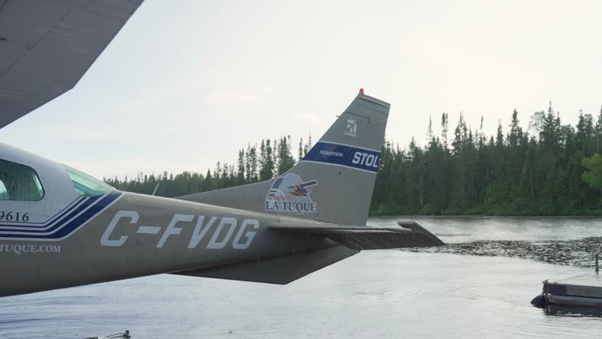 Close fuselage tail of seaplane wing and floats resting on calm lake water surrounded by forest, Seignurie Du Triton Quebec Canada