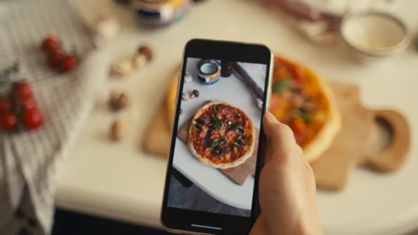 Happy and proud cook takes photos and videos of a successful homemade pizza made from a new recipe learned online, showcasing social media sharing, online learning, and culinary skills.