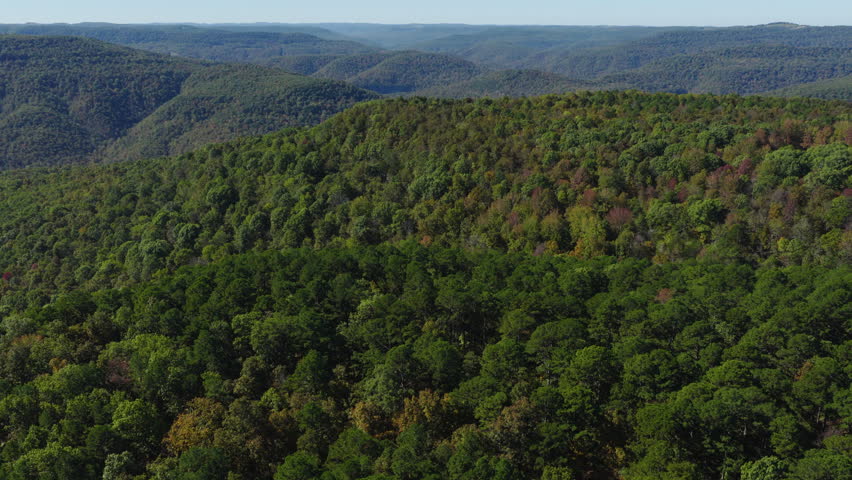 Wide aerial orbit of rolling forested ridges and valleys covered in oak hickory woodland under clear skies, Ozark National Forest Arkansas, fall colors backdrop