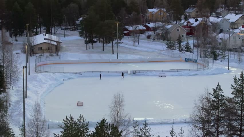 4K cinematic drone footage of two people ice skating in Rovaniemi, Finland, captured at golden hour during the winter solstice._08