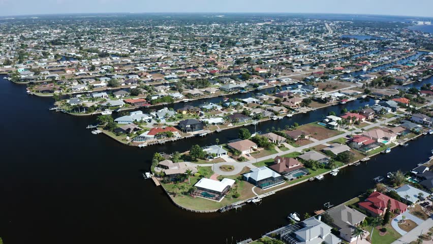 Neighborhood with canals and single-family homes featuring docks and boats located in a sunny, flat environment in Florida, highlighting water access and suburban lifestyle.