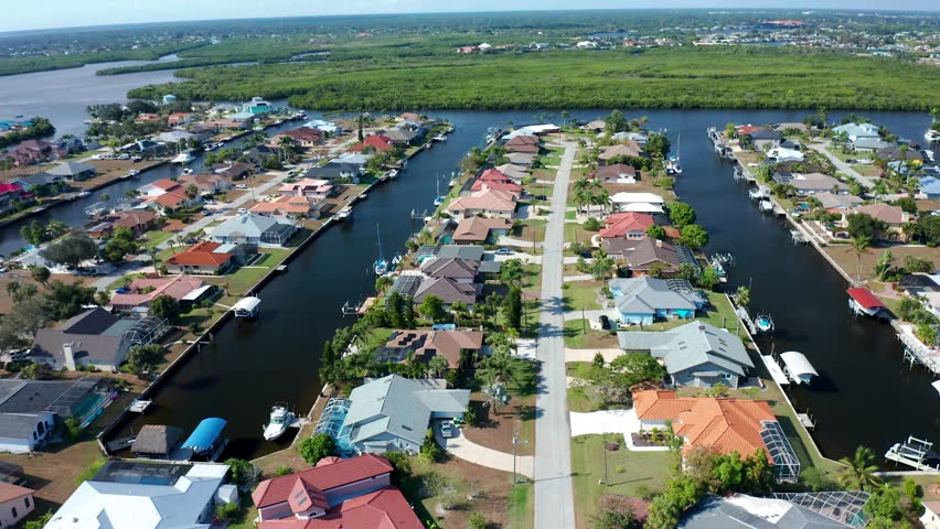Waterfront houses line canals with private boat docks in a sunny residential neighborhood surrounded by lush green landscape and waterways in Florida.