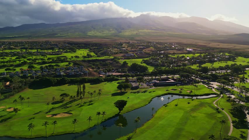 An aerial wide shot captures the expansive, vibrant green fairways of a beautiful golf course in Maui, Hawaii.