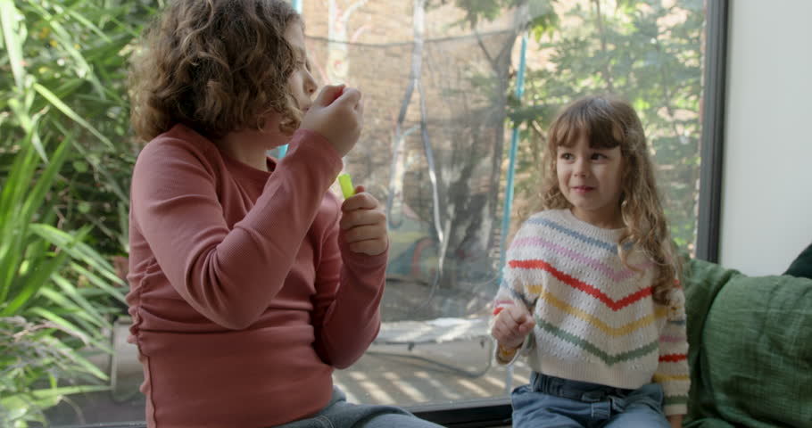 Female Sisters Blowing Bubbles in Living Room