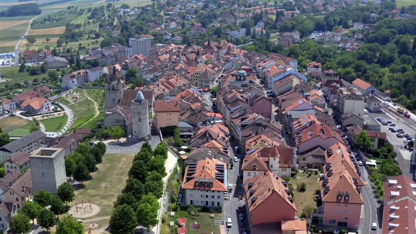 Aerial drone footage of Orbe in the canton of Vaud during summer. Scenic view over the town, historic rooftops and the iconic castle tower under clear blue sky