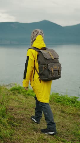 Exploring Nature: A Person in a Yellow Jacket and Backpack Stands by the Water