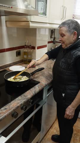 Senior woman with gray hair preparing a healthy meal and stirring vegetables in a frying pan