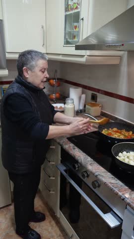 Senior woman stirring vegetables and potatoes in pans on a modern induction cooktop in her kitchen